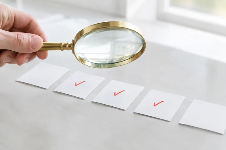 Main tenant une loupe au-dessus de cartes blanches cochées en rouge, vérification d’un profil
